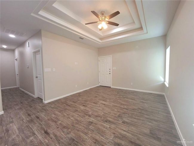 Spare room with a tray ceiling, a ceiling fan, dark wood-type flooring, and baseboards | Image 11