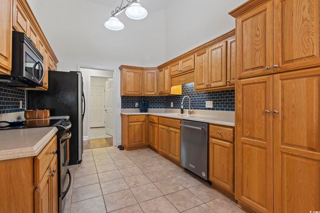Kitchen featuring stainless steel appliances, decorative backsplash, light tile patterned floors, brown cabinetry, and a towering ceiling | Image 14