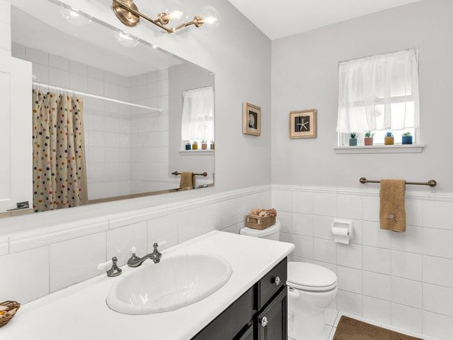 Full bath with toilet, vanity, a shower with shower curtain, tile walls, and a wainscoted wall | Image 16