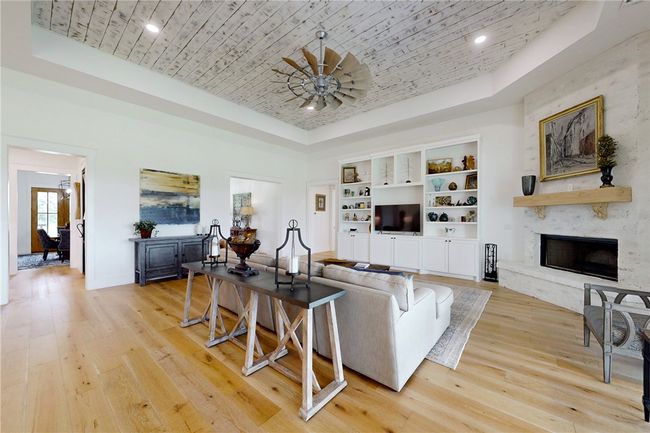 Living area with a raised ceiling, light wood-style floors, a high end fireplace, and recessed lighting | Image 7