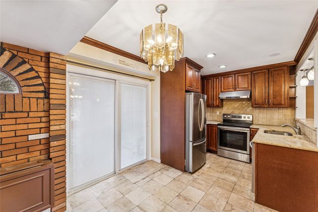 Kitchen featuring tasteful backsplash, appliances with stainless steel finishes, under cabinet range hood, a sink, and light stone counters | Image 4