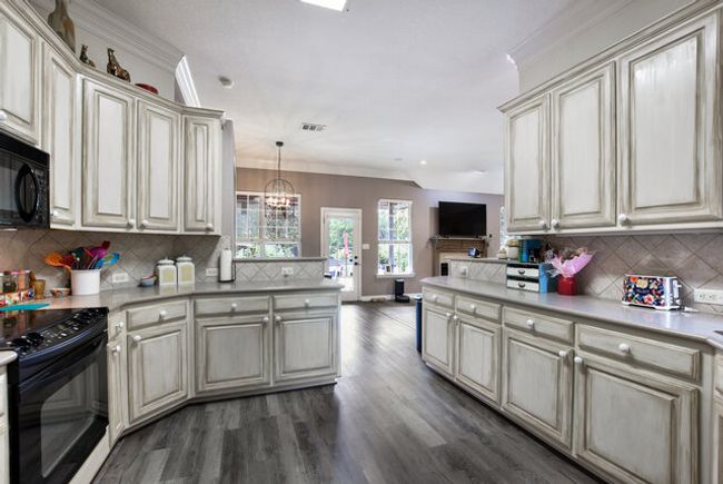 Kitchen featuring black appliances, cream cabinets, a peninsula, dark wood finished floors, and ornamental molding | Image 13
