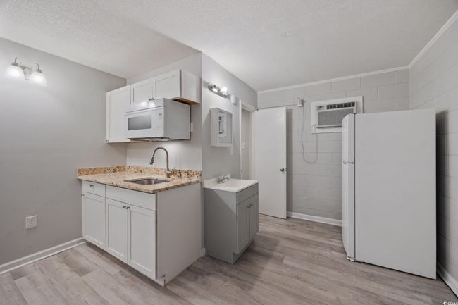 Kitchen with white appliances, a sink, light wood finished floors, a textured ceiling, and a wall unit AC | Image 10