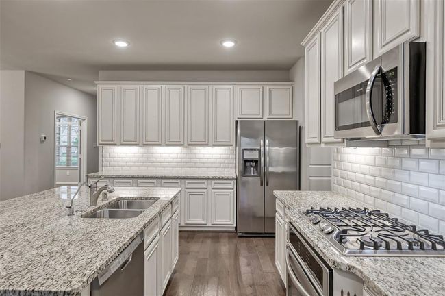 White cabinets and subway tiles brighten this kitchen, featuring stainless steel appliances, granite countertops, and sleek hardwood floors. Modern, airy, and inviting space.... | Image 9
