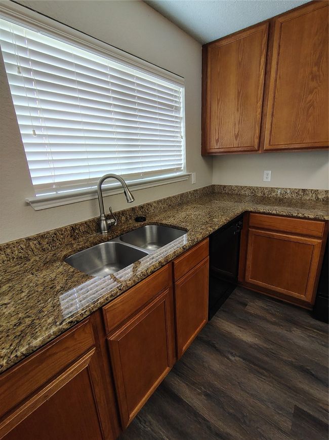 Kitchen featuring a sink, dishwasher, dark wood-style floors, dark stone counters, and brown cabinets | Image 19
