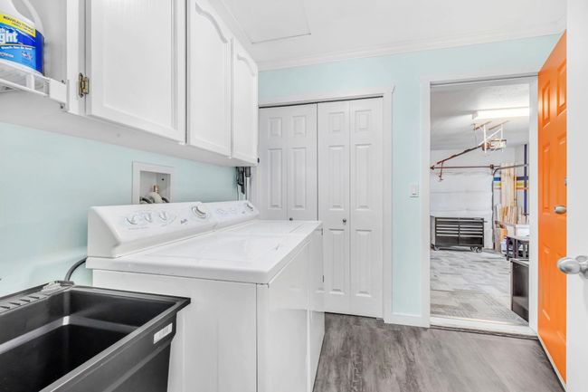 Washroom featuring crown molding, separate washer and dryer, wood finished floors, a sink, and cabinet space | Image 23