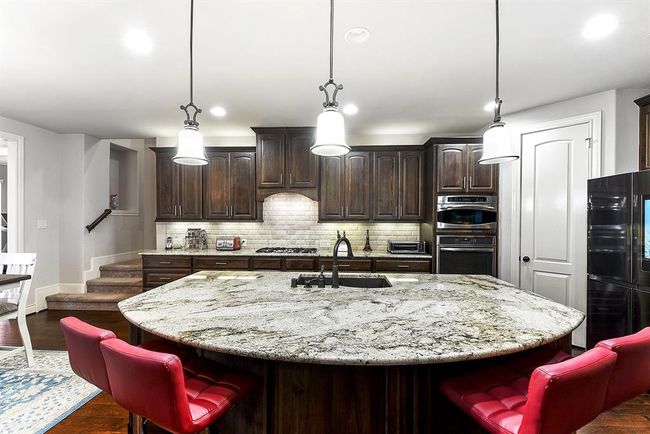 This spacious kitchen offers a great flow and easy access to all three dining areas. The oversized breakfast bar provides plenty of seating, while additional cabinetry offers ample storage space. Pendant lighting beautifully illuminates the area, creating a bright and inviting atmosphere that's perfect for family meals or entertaining guests. | Image 15