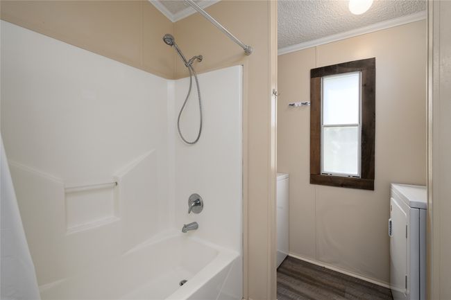 Bathroom with washer / dryer, wood finished floors, a textured ceiling, bathing tub / shower combination, and crown molding | Image 21