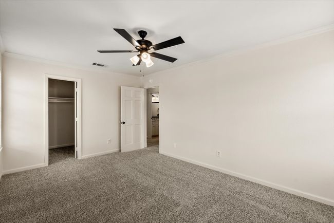 Unfurnished bedroom with ceiling fan, a walk in closet, ornamental molding, and carpet | Image 23