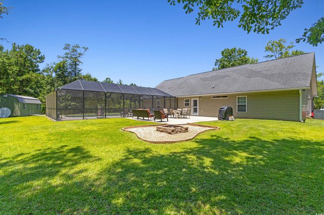 View of grassy yard featuring a fire pit, a patio area, a shed, and glass enclosure | Image 32