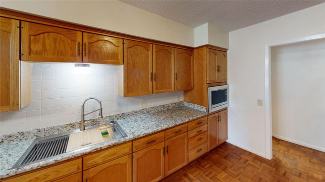 Kitchen with stainless steel microwave, tasteful backsplash, brown cabinets, a textured ceiling, and a sink | Image 4
