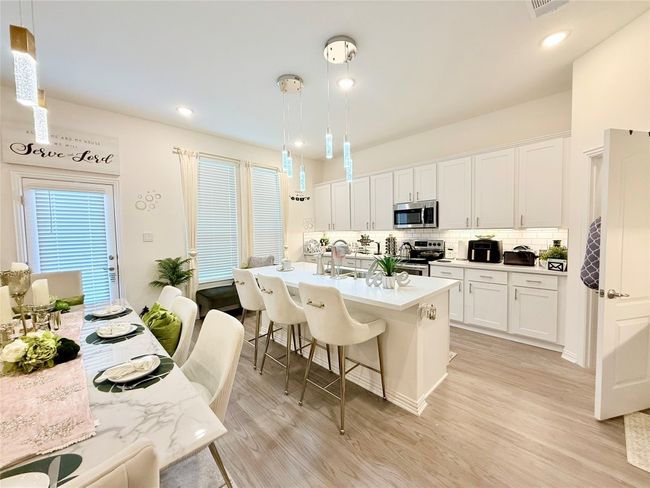 Kitchen with stainless steel appliances, a breakfast bar area, light wood-type flooring, tasteful backsplash, and white cabinets | Image 10