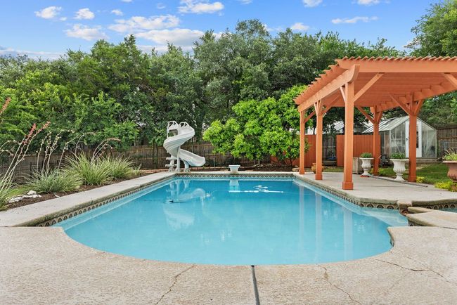 View of swimming pool featuring a water slide, a pergola, a fenced backyard, an outdoor structure, and a patio | Image 6