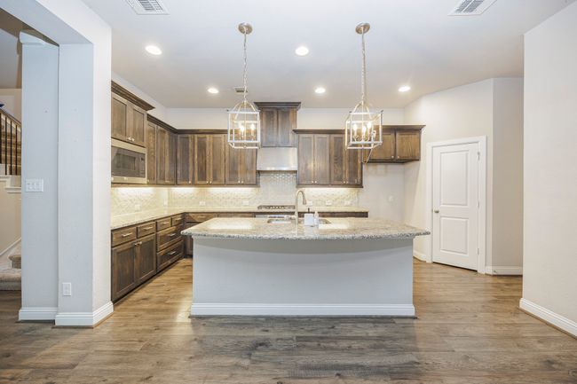 Kitchen featuring stainless steel microwave, a center island with sink, tasteful backsplash, light stone counters, and recessed lighting | Image 17