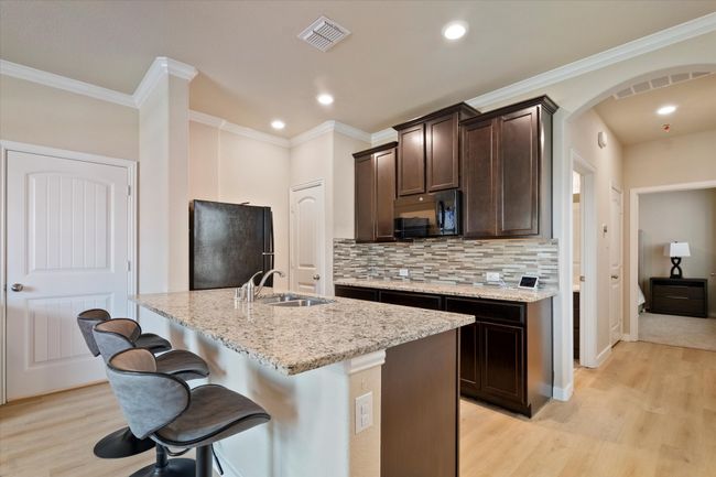 Kitchen featuring black appliances, a sink, light wood finished floors, dark brown cabinetry, and light stone countertops | Image 30