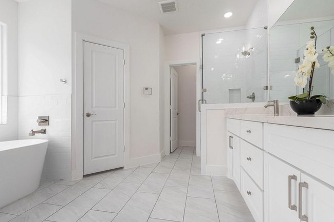 This modern bathroom features a sleek design with a spacious glass shower, a freestanding bathtub, and a double vanity with ample storage. The light color palette and large mirror enhance the bright, airy feel. | Image 22