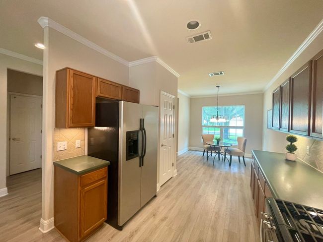 Kitchen with stainless steel fridge, light wood-style floors, decorative backsplash, brown cabinetry, and a chandelier | Image 5