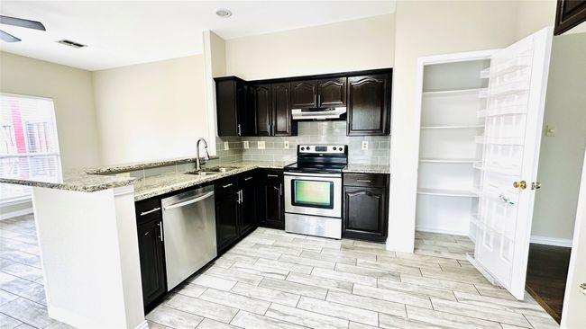 Kitchen featuring stainless steel appliances, under cabinet range hood, a peninsula, light stone counters, and a ceiling fan | Image 5