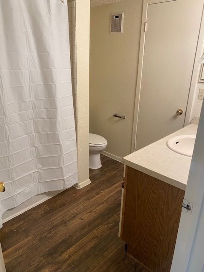Full bath featuring a shower with curtain, vanity, toilet, visible vents, and wood finished floors | Image 11