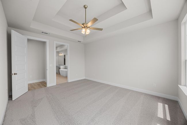 Unfurnished bedroom featuring a raised ceiling, light colored carpet, baseboards, and ensuite bathroom | Image 15