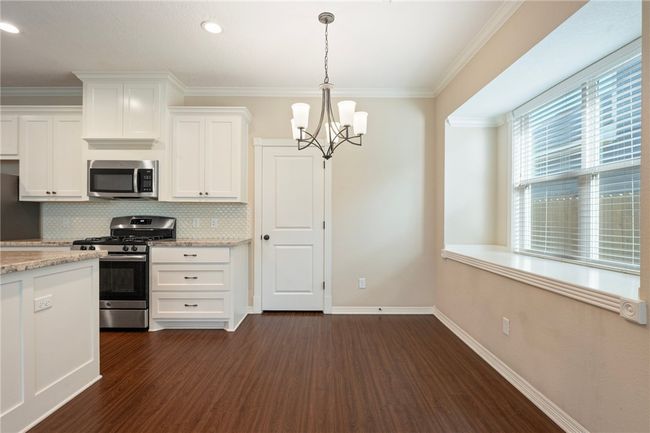 Kitchen featuring appliances with stainless steel finishes, a chandelier, dark wood-type flooring, decorative backsplash, and white cabinetry | Image 6