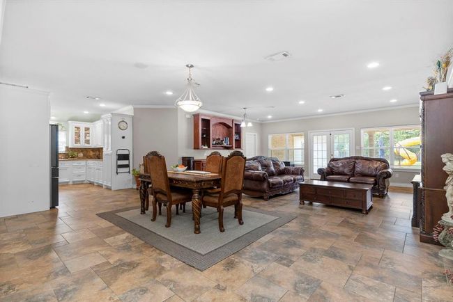 Spacious open-plan living area with tiled flooring, featuring a dining space with a classic wooden table set, a comfortable living room with plush leather seating, and ample natural light from windows overlooking the backyard. | Image 15