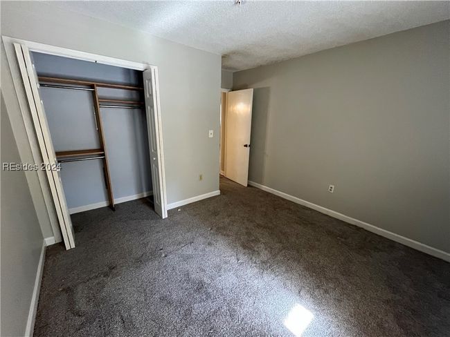 Unfurnished bedroom featuring a closet, a textured ceiling, and dark colored carpet | Image 9