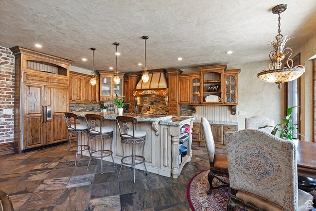 Kitchen with a breakfast bar area, glass insert cabinets, brown cabinetry, and a kitchen island | Image 21