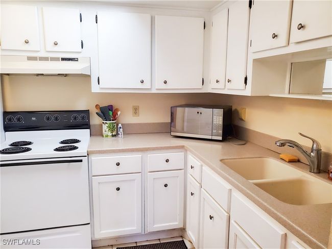 Kitchen with white cabinets, under cabinet range hood, white electric range, and a sink | Image 11