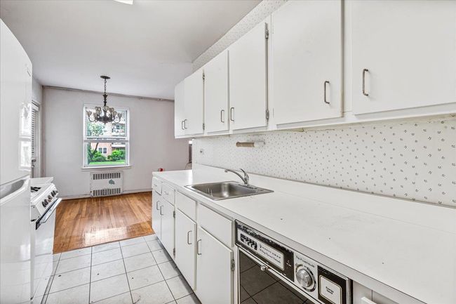 Kitchen featuring radiator, white cabinets, a chandelier, light countertops, and backsplash | Image 9