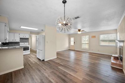 Kitchen with white appliances, ceiling fan with notable chandelier, wood-type flooring, and white cabinetry | Image 1