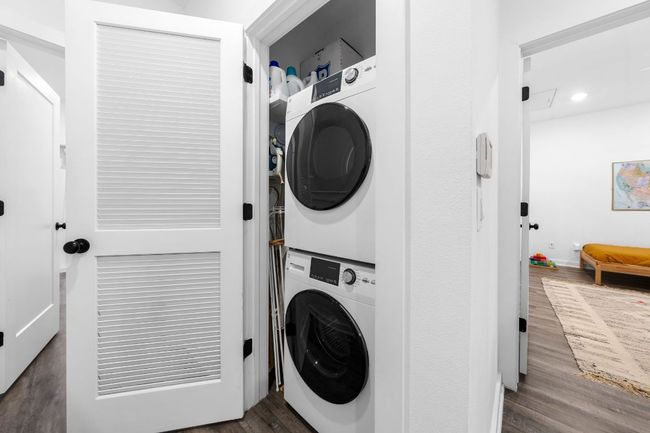 Laundry room with dark wood-type flooring, stacked washing maching and dryer, and laundry area | Image 25