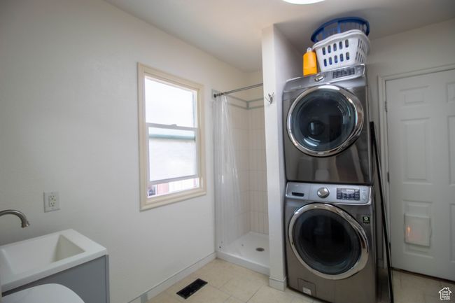 Clothes washing area featuring baseboards, stacked washer and dryer, light tile patterned flooring, visible vents, and a sink | Image 12