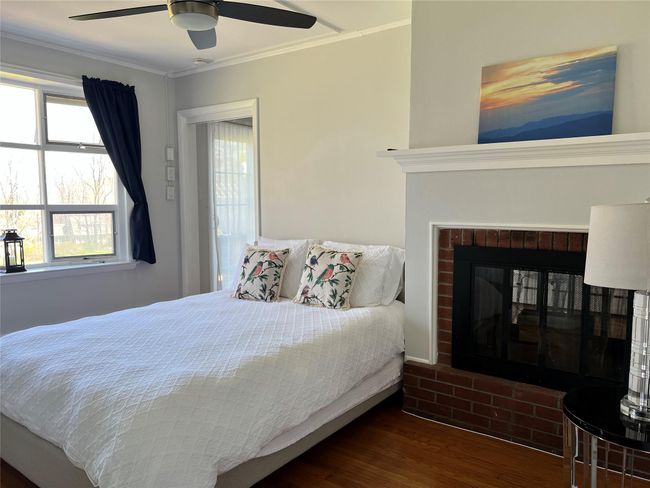 Bedroom featuring a ceiling fan, a brick fireplace, wood finished floors, and crown molding | Image 43