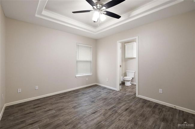 Unfurnished bedroom with a raised ceiling, dark wood-style flooring, connected bathroom, and ceiling fan | Image 6