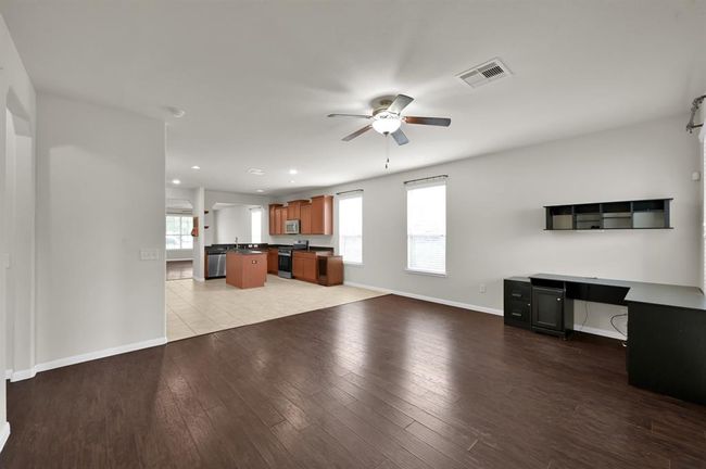 This room features hardwood floors, neutral walls, a ceiling fan, and two large windows offering natural light and a view of the backyard. It's spacious and versatile, perfect for a living area or office. | Image 16