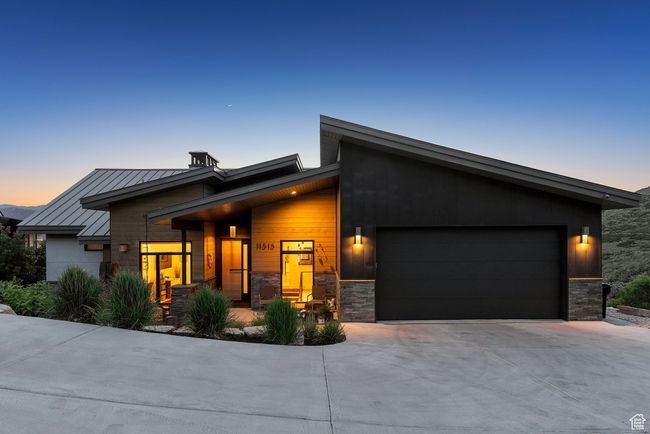 Modern home featuring a garage, driveway, a standing seam roof, stone siding, and a metal roof | Image 97