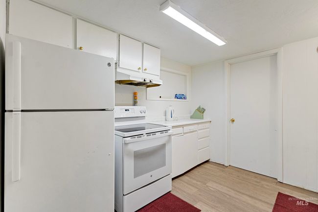 Kitchen with white appliances, under cabinet range hood, light wood-type flooring, light countertops, and white cabinetry | Image 10