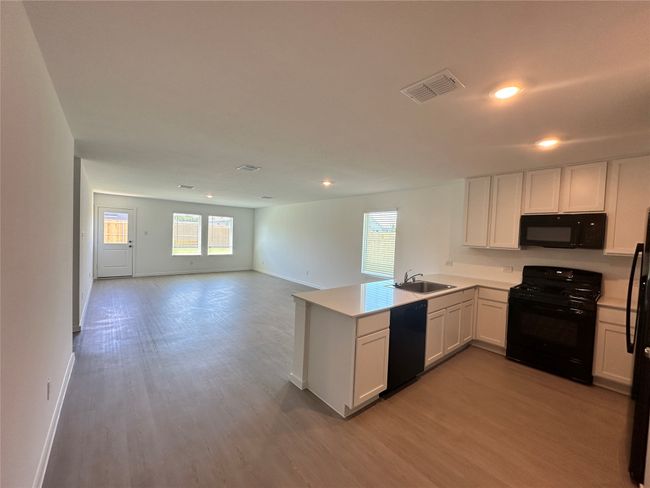 Kitchen with black appliances, a sink, a peninsula, light wood finished floors, and baseboards | Image 5