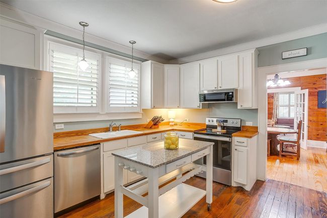 Kitchen with stainless steel appliances, butcher block counters, dark wood-style flooring, white cabinetry, and ornamental molding | Image 25