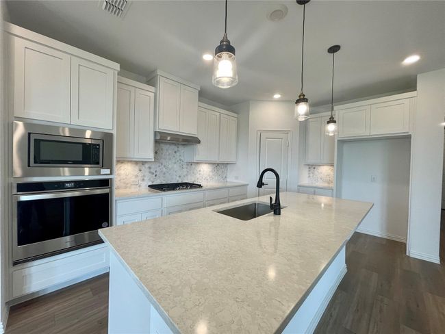 Kitchen featuring appliances with stainless steel finishes, white cabinetry, dark wood-type flooring, decorative backsplash, and recessed lighting | Image 6