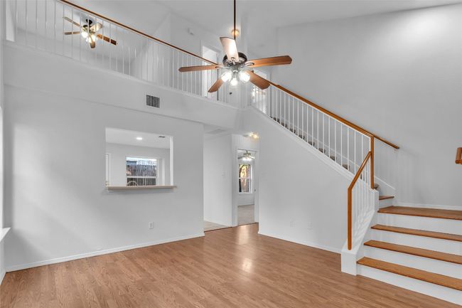 Unfurnished living room with ceiling fan, wood finished floors, stairs, and a high ceiling | Image 9