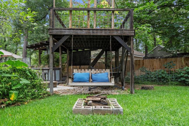 A charming backyard features a cozy wooden deck with a rustic swing underneath. There's a small fire pit surrounded by lush greenery, creating a perfect spot for relaxation and outdoor gatherings. | Image 42