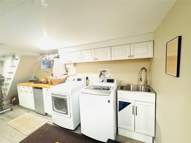 Clothes washing area with cabinet space, light wood-type flooring, washer and dryer, and a sink | Image 15