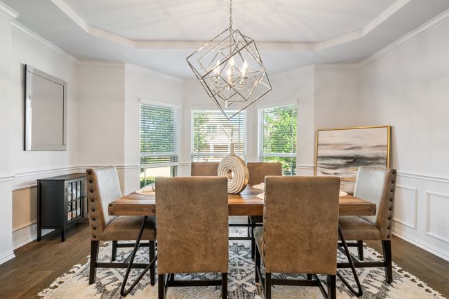 Dining space with a raised ceiling, a chandelier, wood finished floors, a decorative wall, and ornamental molding | Image 9