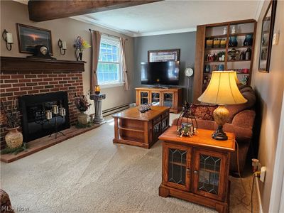 Carpeted living room featuring baseboard heating, a brick fireplace, and crown molding | Image 2