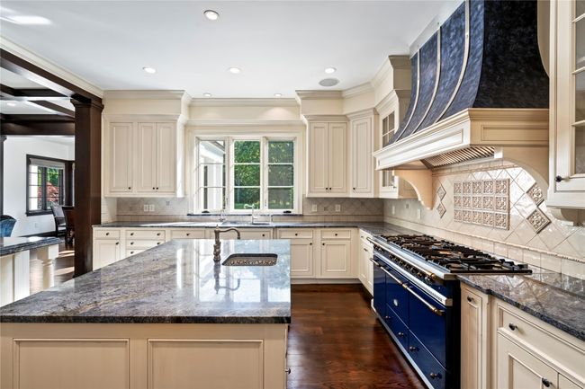 Kitchen featuring dark stone counters, cream cabinets, a center island with sink, gas stove, and custom range hood | Image 6