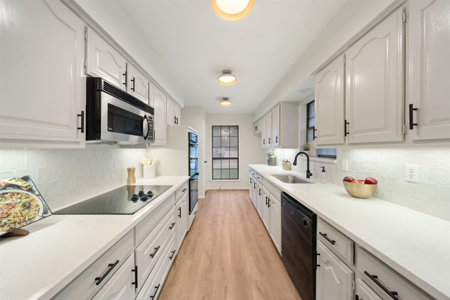 Kitchen featuring quartz countertops, a farm sink, light wood-style flooring, dishwasher, double oven and a tile backsplash | Image 6