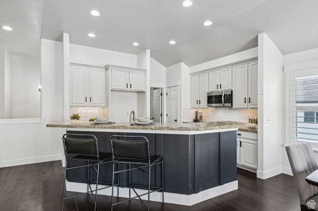 Kitchen with light stone countertops, vaulted ceiling, a center island with sink, a breakfast bar, and tasteful backsplash | Image 10