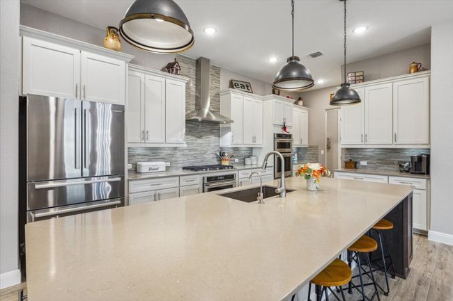 Kitchen featuring stainless steel appliances, wall chimney range hood, light wood look tile flooring, a large island, and white cabinets | Image 15